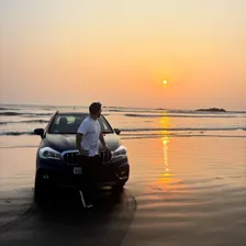 Prasenjit leaning on his car on a beach at sunset